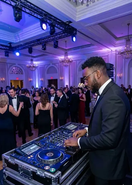 DJ professionnel mixant lors d'un mariage élégant sous un éclairage violet chaleureux, avec des invités chics dansant en arrière-plan